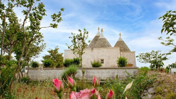A building with a unique architectural style, featuring three conical roofs and a stone wall surrounding the property.