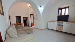 A living room with a sofa, a TV, and a kitchen area with cabinets and a window.