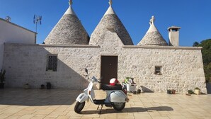A stone building with three conical roofs, a white scooter parked in front, and a door with a small window.