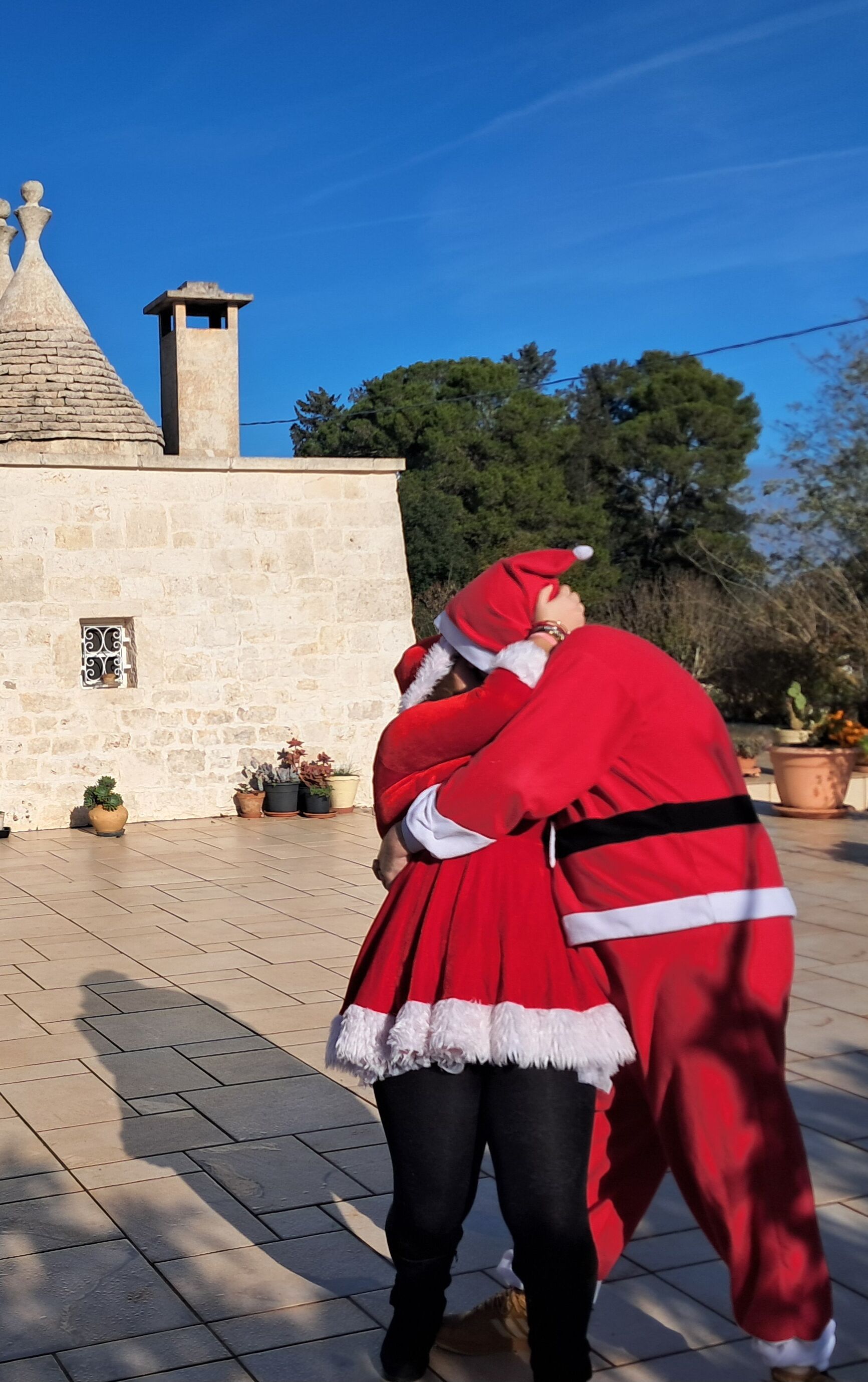 A person in a red Santa costume standing in front of a stone building with a tiled roof and a chimney.