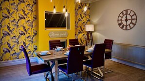 A dining area with a yellow wall, a clock, and a 'Be our guest' sign.