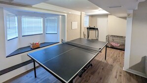 Una habitación con mesa de ping pong, cinta de correr y jaula con una manta rosa.
