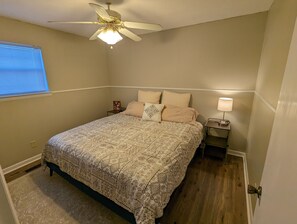 A bedroom with a bed, a ceiling fan, a nightstand, a lamp, and a window with blinds.