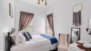 A bedroom with a bed, curtains, a bedside table, a mirror, and a wall-mounted light fixture. - Charming, cozy, vintage house located in the historic Silver Valley. (Mullan)