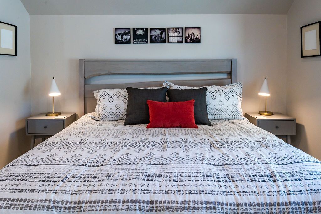 Una cama bien hecha con ropa de cama estampada, dos lámparas de noche y una pared con cuadros.
