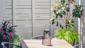 A wooden table with metal chairs, a potted plant, and a metal lantern in a patio area. - Courtside Cottage - WalkScore 93 - Dog Friendly (Ashland)