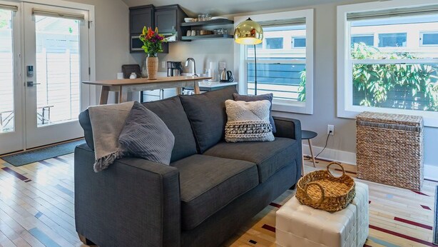 A modern living room with a grey sofa, a small table, and a basket on a white ottoman. - Courtside Cottage - WalkScore 93 - Dog Friendly (Ashland)