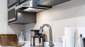 A modern kitchen with a stainless steel coffee maker, a kettle, and a sink. - Courtside Cottage - WalkScore 93 - Dog Friendly (Ashland)