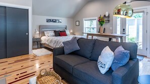 A modern bedroom with a large bed, a grey sofa, and a dining area. - Courtside Cottage - WalkScore 93 - Dog Friendly (Ashland)