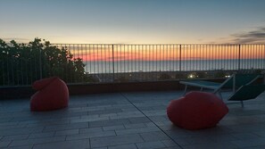 A rooftop terrace with a view of the sunset over the sea, featuring two red bean bags and a green lounge chair. - HOTEL SANTANNA (Rimini)