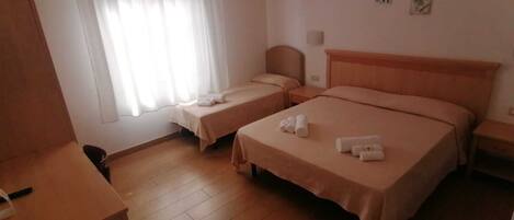 A hotel room with two single beds, a wooden desk, a chair, and a window with sheer curtains.