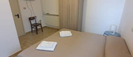 A hotel room with a bed, a chair, a television, an air conditioning unit, and a door.
