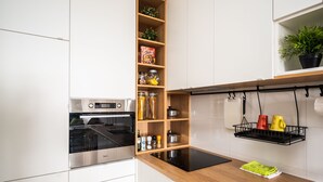 Et moderne køkken med hvide skabe, en træreol, en sort induktionskogetop og en ophængt grydeholder.