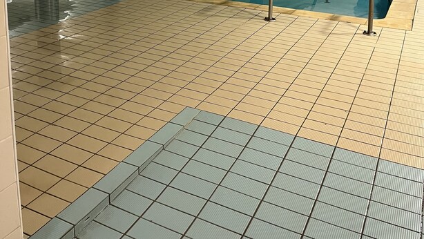An indoor swimming pool with tiled floors and walls, blue pillars, and metal railings. - Lodging in the woods (Les Deserts)