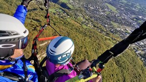 A person paragliding with a helmet and harness, overlooking a mountainous landscape with a village below. - Lodging in the woods (Les Deserts)