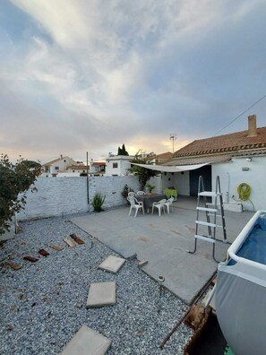 A residential backyard with a swimming pool, a patio with outdoor furniture, and a white wall.