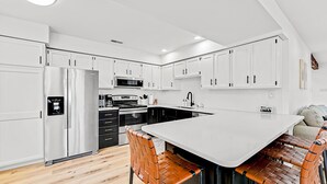 Een moderne keuken met witte kastjes, een roestvrijstalen koelkast, een magnetron en een groot eiland met een spoelbak.
