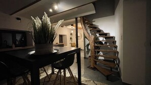 Un interior moderno con zona de comedor que presenta una mesa y sillas de madera oscura, una planta en maceta y una escalera con escalones de madera.