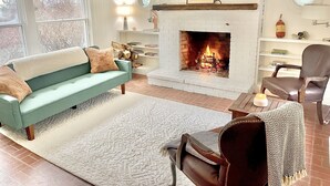 A living room with a white brick fireplace, a green sofa, a brown leather chair, and a wooden coffee table.