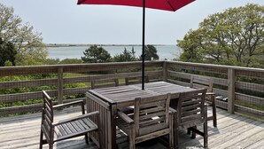 A wooden deck with a table and chairs, a red umbrella, and a view of the water.