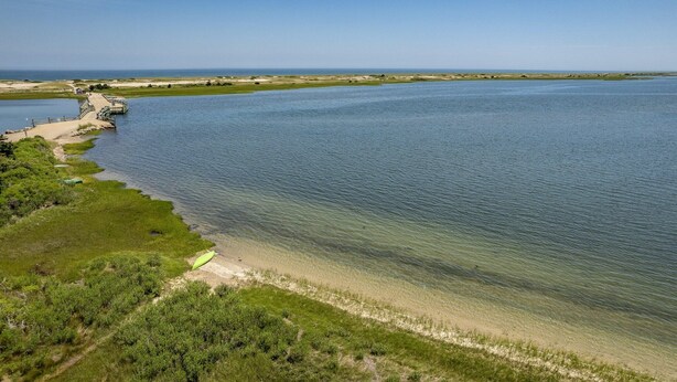 An aerial view of a coastal area with a clear water body, a sandy beach, and a small structure near the water's edge.