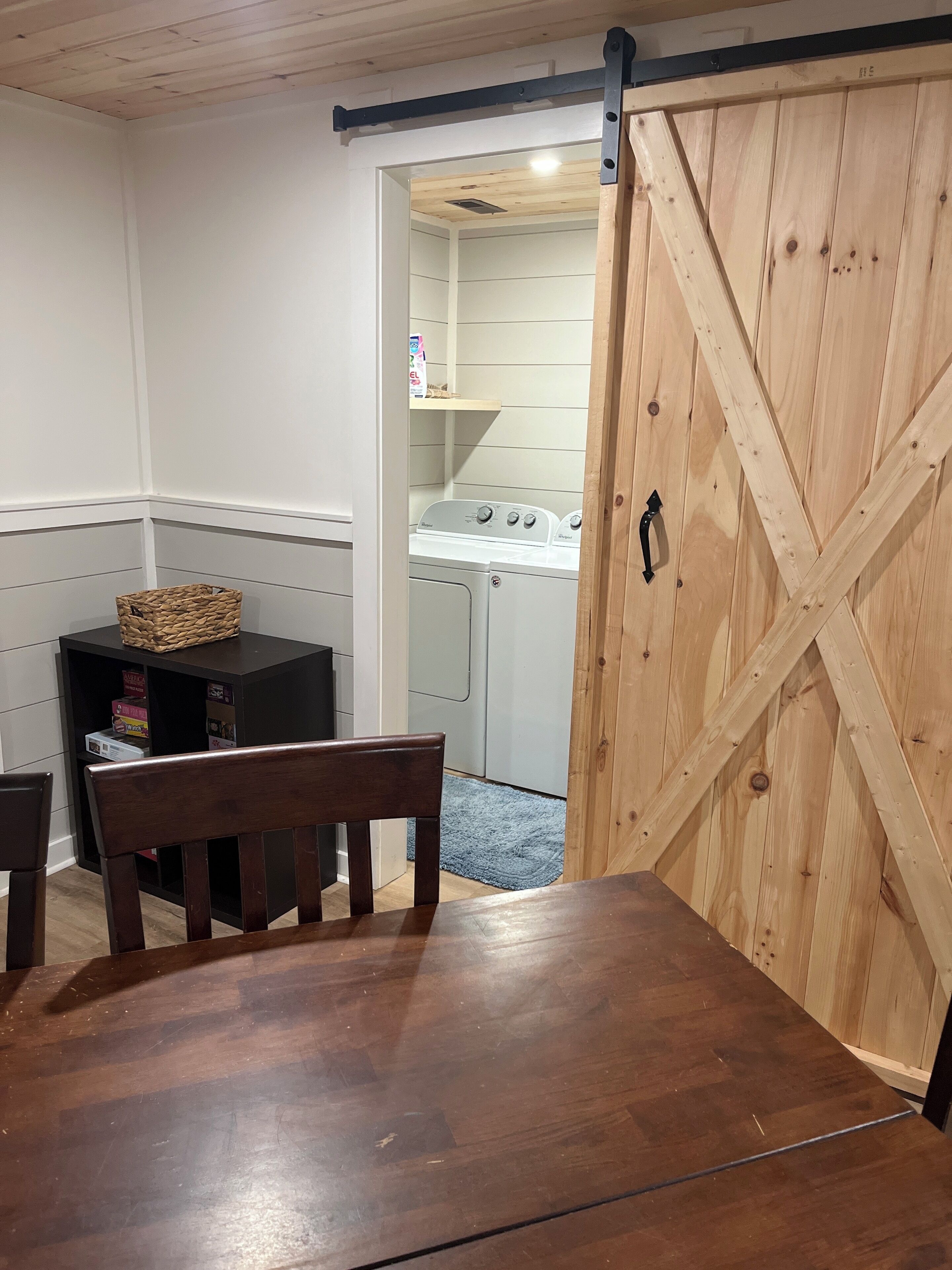 Ein Zimmer mit Holztisch, einem Stuhl, einer Waschmaschine und einer Schiebetür im Bauernhausstil.