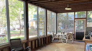 Une véranda avec de grandes fenêtres, un plafond en bois, une table à manger avec des chaises et une petite table avec une chaise.