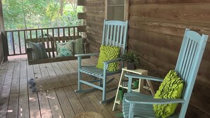 Une véranda en bois, avec des fauteuils à bascule et une petite table, entourée de murs en bois et offrant une vue sur la verdure.