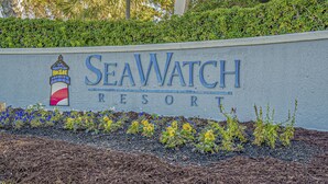 Letrero del SeaWatch Resort con logotipo de faro, rodeado por un área ajardinada con mantillo y plantas.