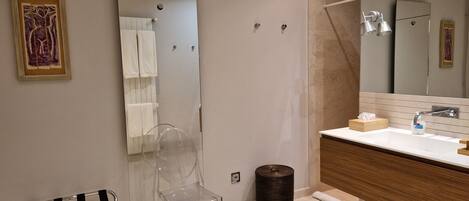 A modern bathroom with a large mirror, a sink with a wooden vanity, a clear chair, and a towel rack.