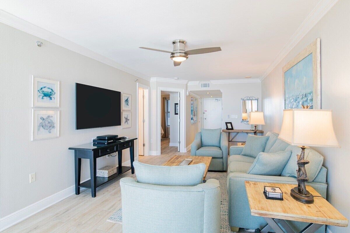 A modern living room with a flat-screen TV, a ceiling fan, and light blue furniture.