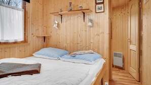 Une pièce en bois avec un lit, une étagère ornée d’objets décoratifs, un luminaire fixé au mur et une porte.