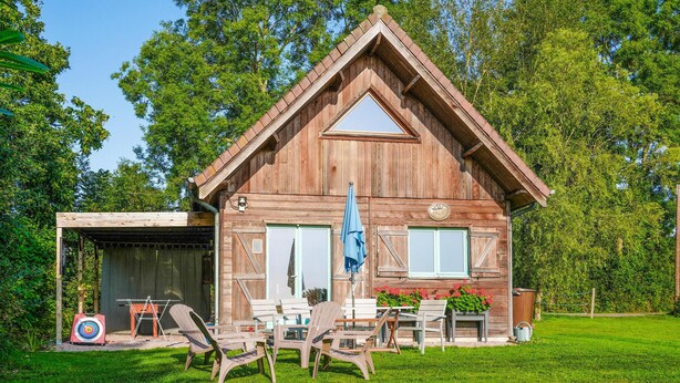 Une cabane en bois avec un toit à deux versants, une véranda et un petit espace extérieur aménagé avec des chaises et une table.