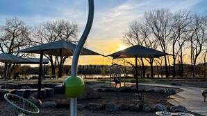 A park with a playground, seating areas, and a body of water in the background.