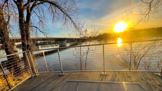 A metal railing overlooking a river with a bridge in the background.