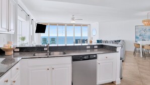 A modern kitchen with white cabinetry, a granite countertop, and a built-in dishwasher. - Crystal Shores West 1401 | Guest Favorite! Gorgeous updates! Endless views! (Gulf Shores)