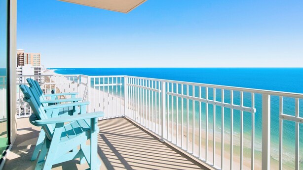 A balcony with a view of the ocean, a white railing, and two blue Adirondack chairs. - Crystal Shores West 1401 | Guest Favorite! Gorgeous updates! Endless views! (Gulf Shores)
