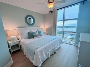 Une chambre avec un grand lit, une table de chevet, un ventilateur de plafond, une vue sur l’eau et une fenêtre.