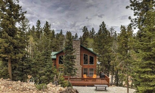 Una cabaña con chimenea de piedra, fachada de madera y una terraza con sillas.