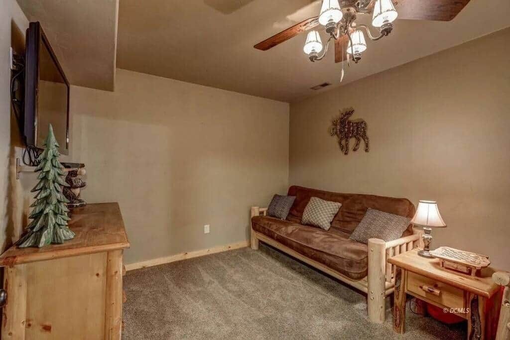 A cozy living room with a brown sofa, a small wooden table with a lamp, and a ceiling fan.