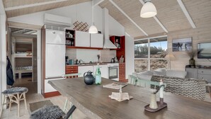 Una cuina moderna amb una illa central, bigues de sostre de fusta i un gran finestral amb vista a un paisatge natural.