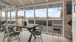 Una habitació àmplia amb una taula gran i cadires, grans finestres que ofereixen vista del paisatge i un sostre de fusta.