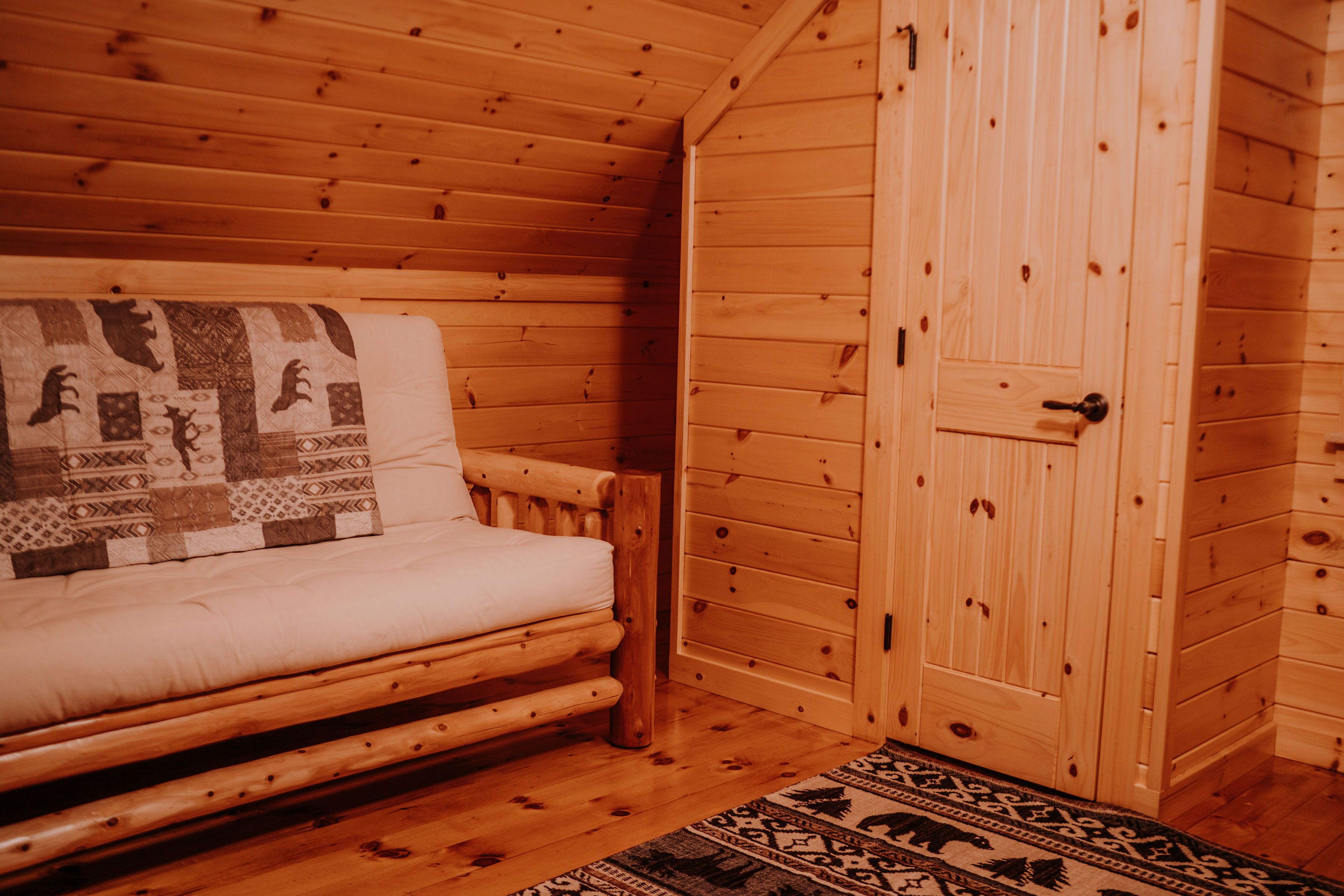 A log cabin room with a wooden bed, a quilt, and a wooden wardrobe.