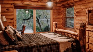 Camera da letto in baita di legno con un letto, una sedia, una finestra e una ventola a soffitto.