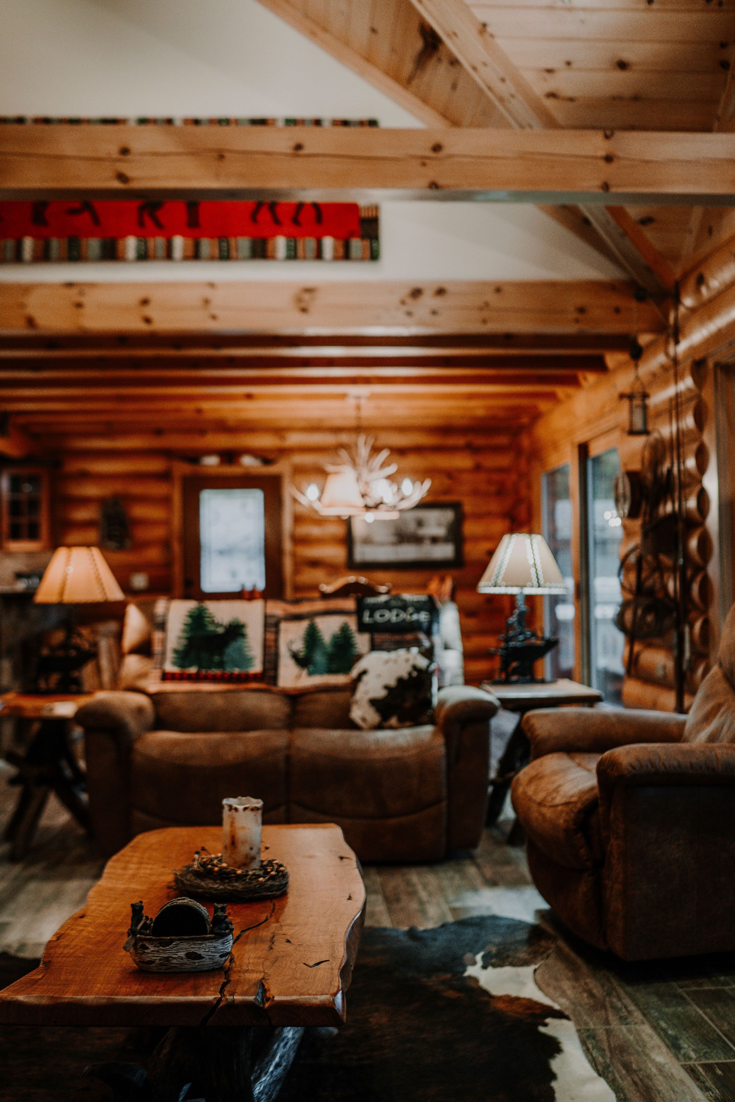 L’intérieur d’un chalet confortable, avec un plafond en bois, une cheminée, un canapé et une table basse agrémentée d’objets décoratifs.