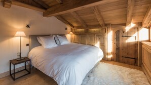 Ein Schlafzimmer mit Holzbalkendecke, einem Bett mit weißer Bettwäsche, einem kleinen Nachttisch mit Lampe und einem flauschigen weißen Teppich.