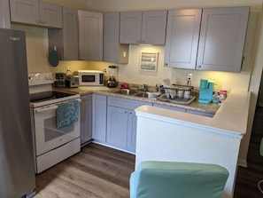 A compact kitchen with light grey cabinets, a white refrigerator, a microwave, a stove, and a small sink.