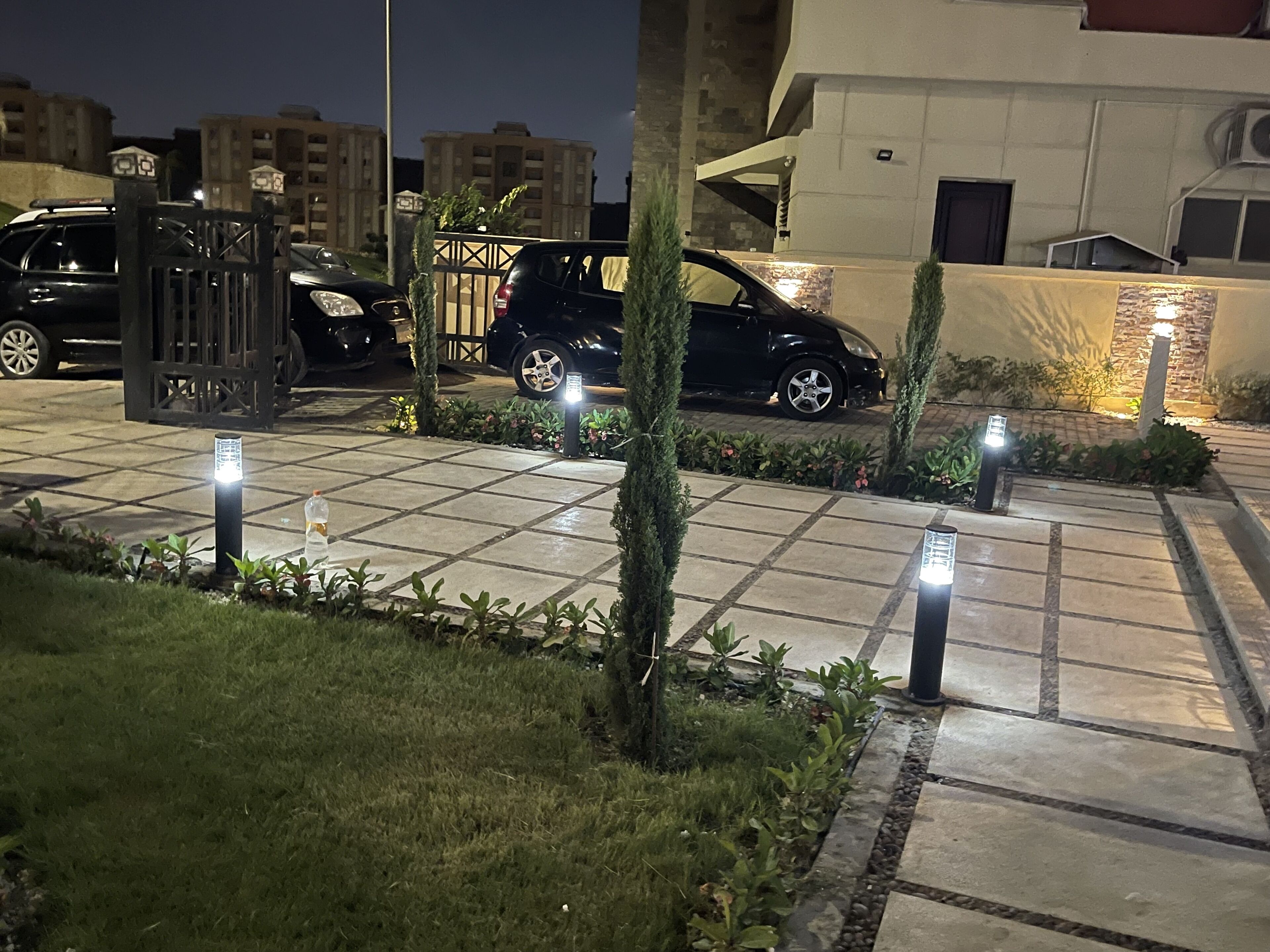 Un estacionamiento cerrado con un camino pavimentado, rodeado de vegetación e iluminado por luces en el suelo.