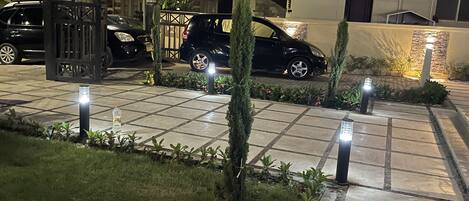 Un estacionamiento cerrado con un camino pavimentado, rodeado de vegetación e iluminado por luces en el suelo.