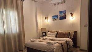 Un lit bien fait, avec une tête de lit, une lampe de chevet et deux appliques murales.